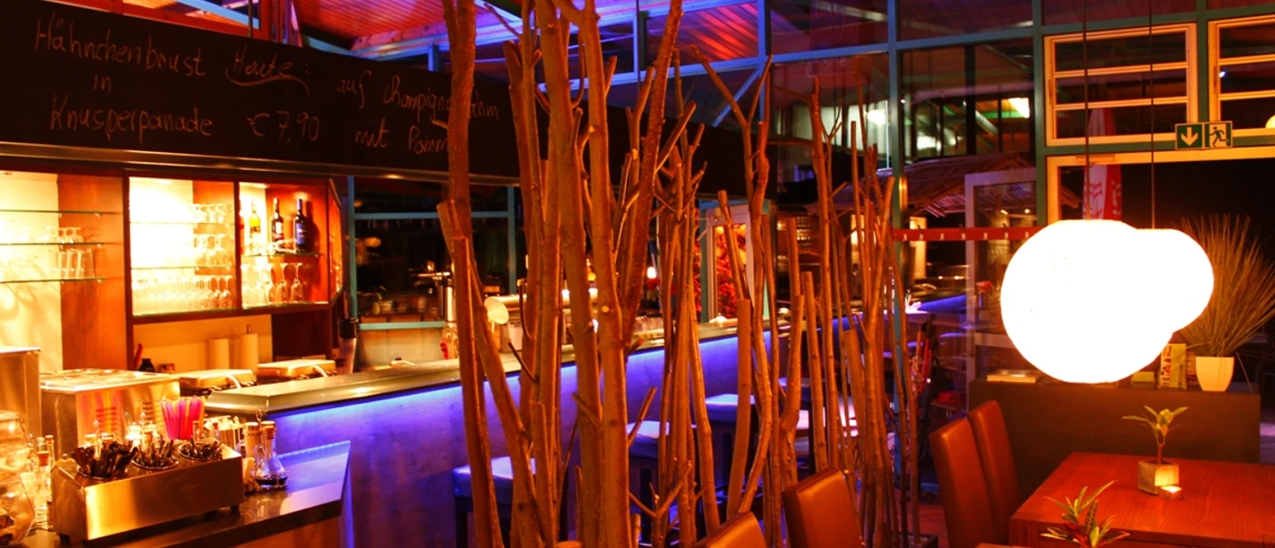 Ein stilvoll beleuchteter Barbereich mit farbigem Licht, modernen Holzmöbeln und dekorativen Zweigen.