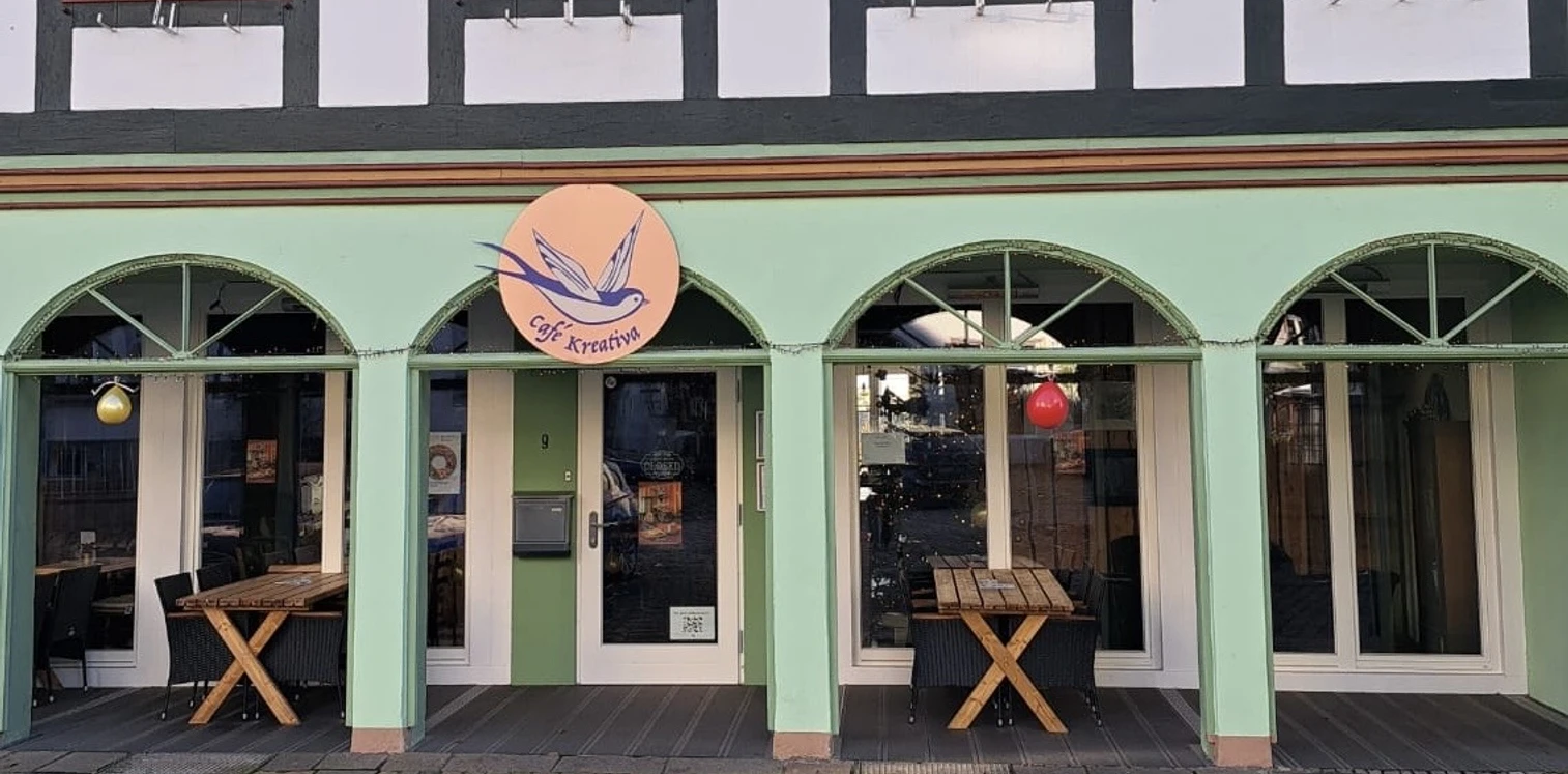 Die Fassade eines Fachwerkhauses mit vier grünen Rundbogenfenstern und einem leuchtenden Café-Schild.