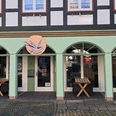 1b4c911c-d858-4fb6-b3b0-0cdaa397952b.jpg Die Fassade eines Fachwerkhauses mit vier grünen Rundbogenfenstern und einem leuchtenden Café-Schild.