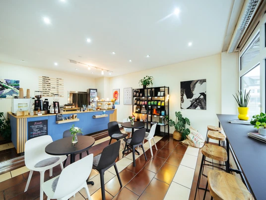 Kaffeerösterei Beanlab Eine moderne Kaffeerösterei mit Sitzgruppen, Regalen voller Kaffeeprodukte und Pflanzen im Raum.