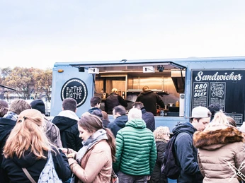 Street Food Festival Köln Ein lebendiges Street-Food-Festival. Menschen stehen in einer Schlange vor einem Food-Truck, der leckere Sandwiches anbietet. A lively street food festival. People queue up in front of a food truck offering delicious sandwiches.