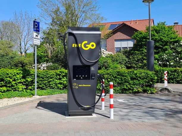 Ladesäule am Kögel-Willms-Platz Ladesäule für Elektroautos auf einem Parkplatz, umgeben von Grün und Wohnhäusern bei Sonnenschein.