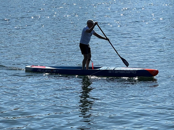 Stand Up Paddling.jpg Person auf einem Stand-up-Paddle-Board bei sonnigem Wetter auf einem ruhigen See paddelnd.