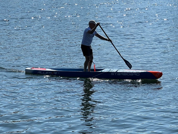 Stand Up Paddling.jpg Person auf einem Stand-up-Paddle-Board bei sonnigem Wetter auf einem ruhigen See paddelnd.