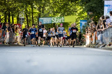 Personen in Laufkleidung mit Startnummern laufen unter einem Banner mit der Aufschrift "START" durch.