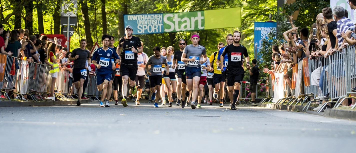 Personen in Laufkleidung mit Startnummern laufen unter einem Banner mit der Aufschrift "START" durch.