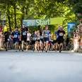 Lousberglauf (c) Sarah Rauch.jpg Personen in Laufkleidung mit Startnummern laufen unter einem Banner mit der Aufschrift "START" durch.