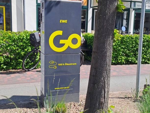 EWE-Go-Ladesäule am Gehweg vor einem Antiquitäten- und Vintage-Geschäft.