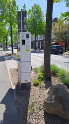 EWE-Go-Ladesäule an einer baumbestandenen Straße mit parkenden Autos.