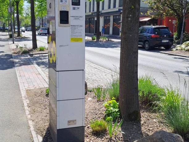 EWE-Go-Ladesäule an einer baumbestandenen Straße mit parkenden Autos.