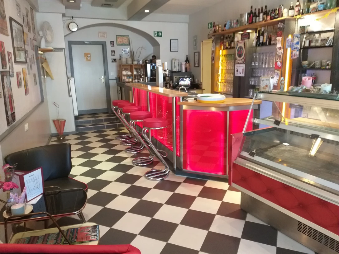 Retro-Style-Bar mit rot beleuchteter Theke, rotem Barhocker, schwarz-weiß karierten Boden.