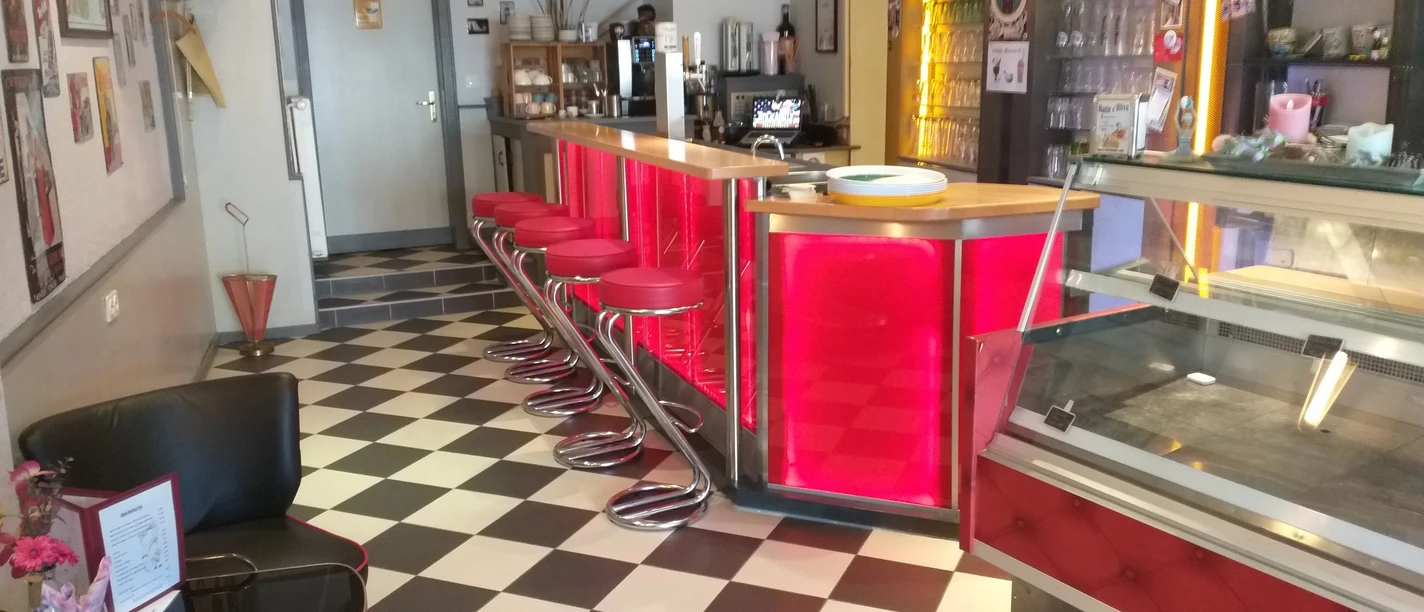 Retro-Style-Bar mit rot beleuchteter Theke, rotem Barhocker, schwarz-weiß karierten Boden.