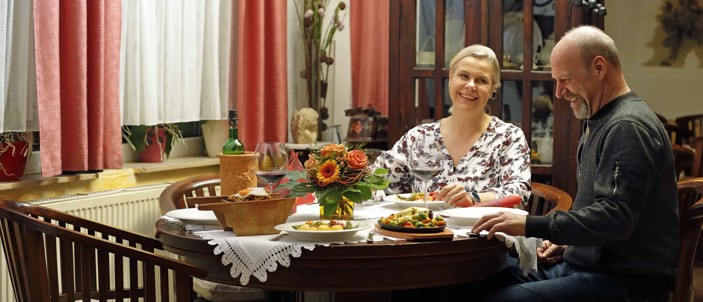 Ein Paar sitzt an einem runden Holztisch in einem traditionell dekorierten Raum und speist.