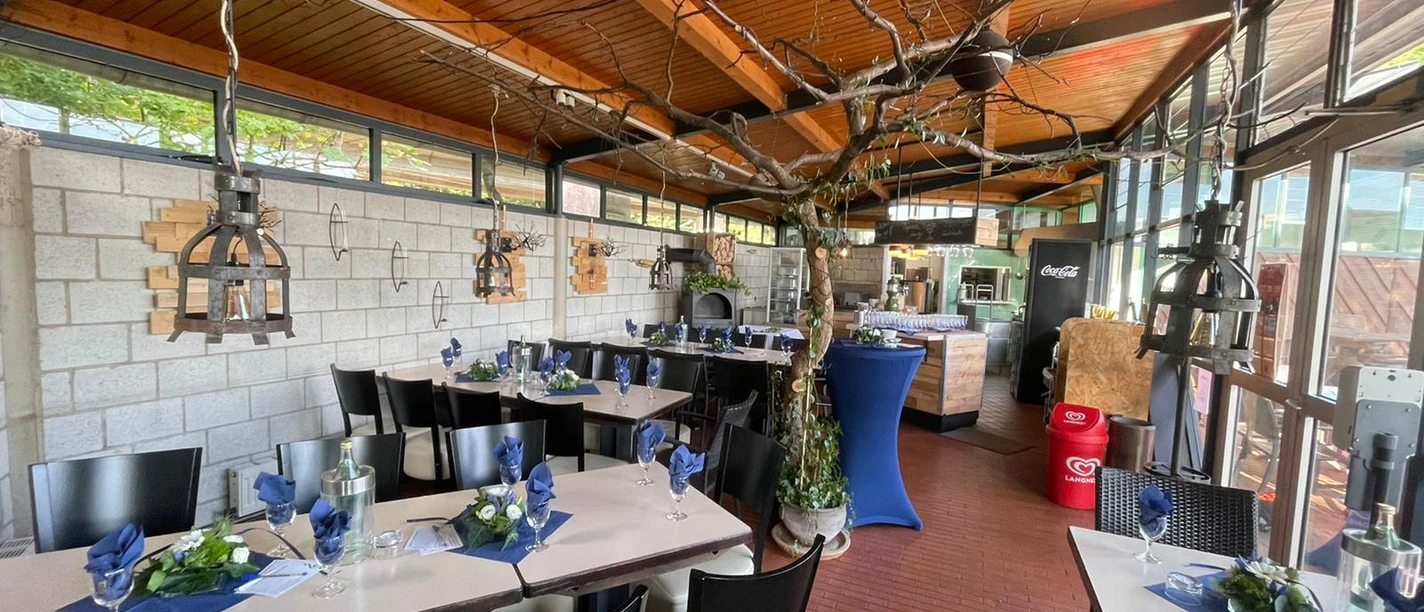 Ein luftiger Raum mit Holzdecke, elegant gedeckten Tischen und einem rustikalen Ofen als Blickpunkt.