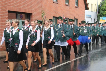 Schützenfest-Hagenburg-Ausmarsch Parade von Schützen in grünen Uniformen mit Abzeichen marschiert an einem regenverhangenen Tag.