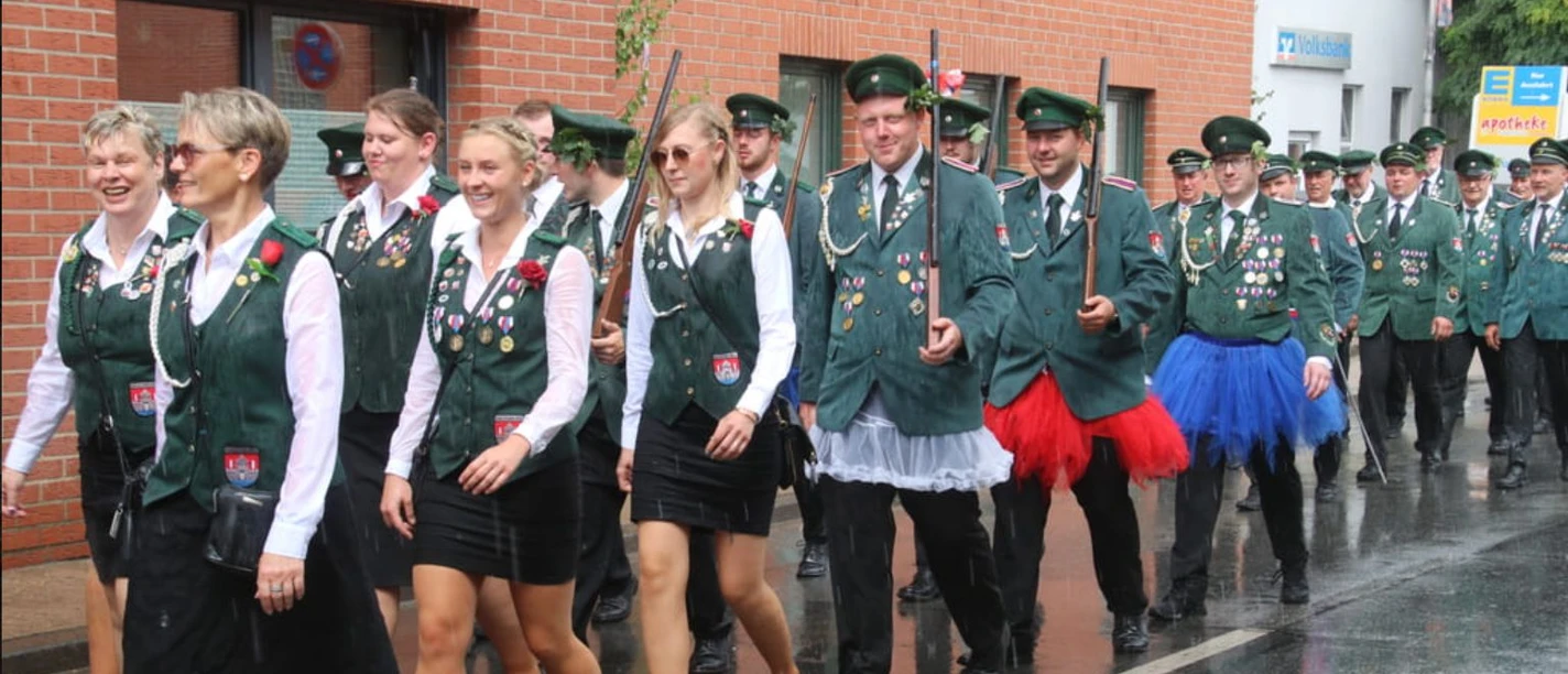 Schützenfest-Hagenburg-Ausmarsch Parade von Schützen in grünen Uniformen mit Abzeichen marschiert an einem regenverhangenen Tag.