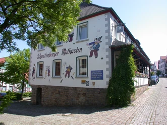 Schwalenberger Malkasten1.JPG Fachwerkgebäude mit Wandbemalung und Figurendekor. Kopfsteinpflaster und sonnige Umgebung ergänzen das Bild.