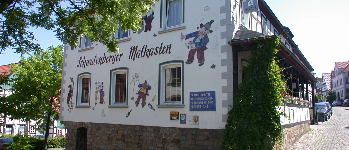 Schwalenberger Malkasten1.JPG Fachwerkgebäude mit Wandbemalung und Figurendekor. Kopfsteinpflaster und sonnige Umgebung ergänzen das Bild.