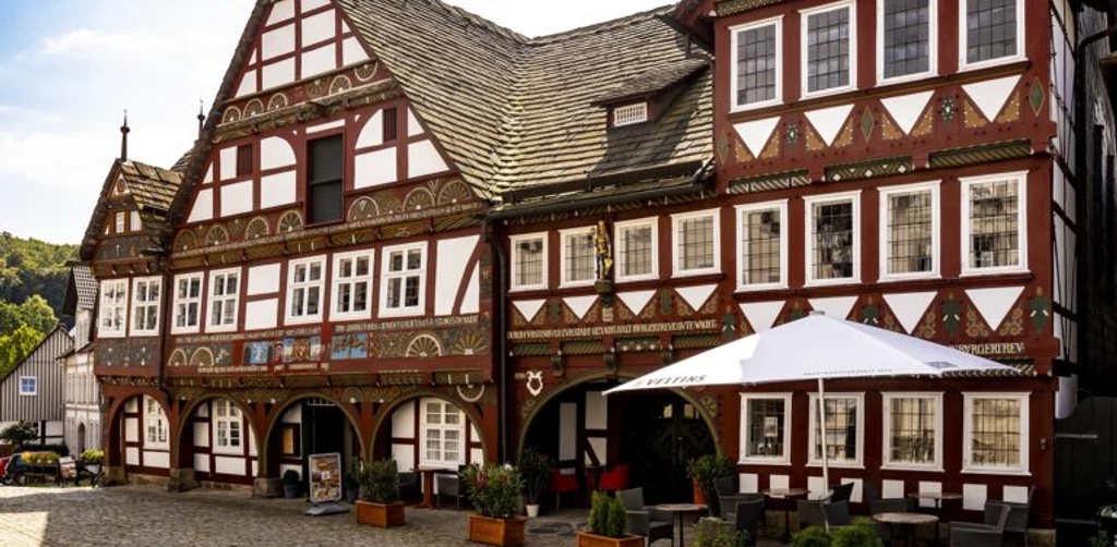 Historisches Fachwerkhaus mit verzierten Fassaden, Arkadengang und Außensitzbereich auf gepflastertem Platz.