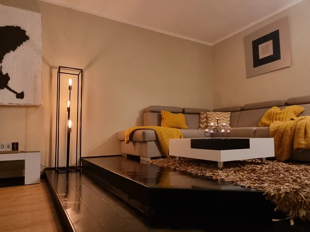 Wohnzimmer (2).jpg Ein gemütliches Wohnzimmer mit einem großen, beigen Sofa, gelben Decken und modernen Kunstwerken.