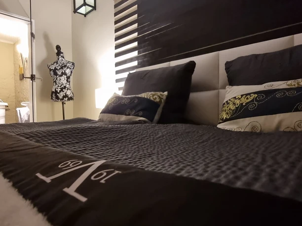 Schlafzimmer.jpg Ein Doppelbett in einem modernen Schlafzimmer, dekoriert mit Kissen, Blick in ein angrenzendes Badezimmer.