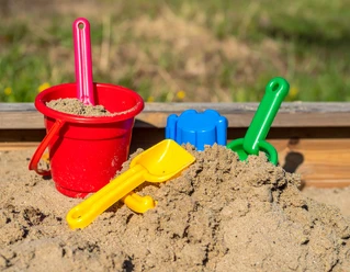Spielplätze bei Den westfälischen Sieben Ein Sandkasten voller Spielzeug mit einem roten Eimer, gelbem und grünem Spaten.
