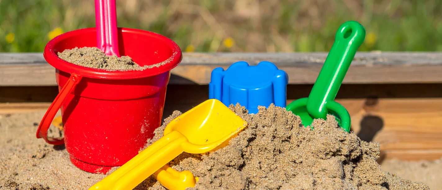 Spielplätze bei Den westfälischen Sieben Ein Sandkasten voller Spielzeug mit einem roten Eimer, gelbem und grünem Spaten.