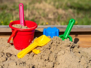 Spielplätze bei Den westfälischen Sieben Ein Sandkasten voller Spielzeug mit einem roten Eimer, gelbem und grünem Spaten.