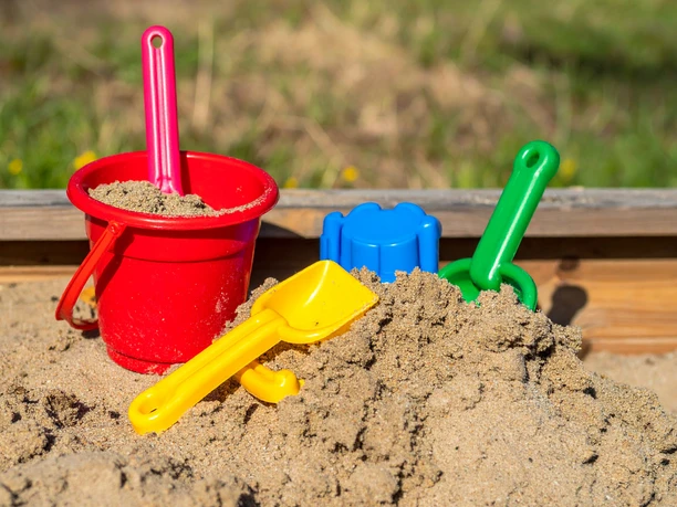 Spielplätze bei Den westfälischen Sieben Ein Sandkasten voller Spielzeug mit einem roten Eimer, gelbem und grünem Spaten.