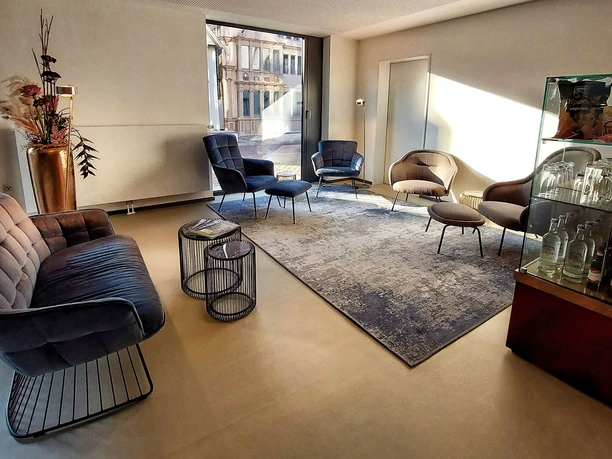 Moderne Hotel-Lobby mit stilvollen Sesseln, großem Teppich und Vitrine mit Likören und Weinen.