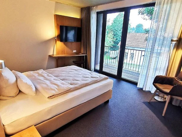Geräumiges Hotelzimmer mit einem Queen-Size-Bett, bodentiefen Fenstern und einem Balkon mit Ausblick.