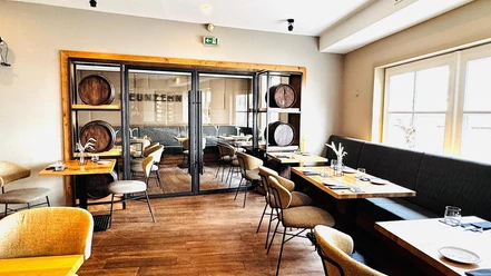 NUENZEHN01_Restaurant_hinten.jpg Innenansicht Gastraum mit Holzfußboden, langer Polstersitzbank rechts, Tischen und Stühlen, modern
