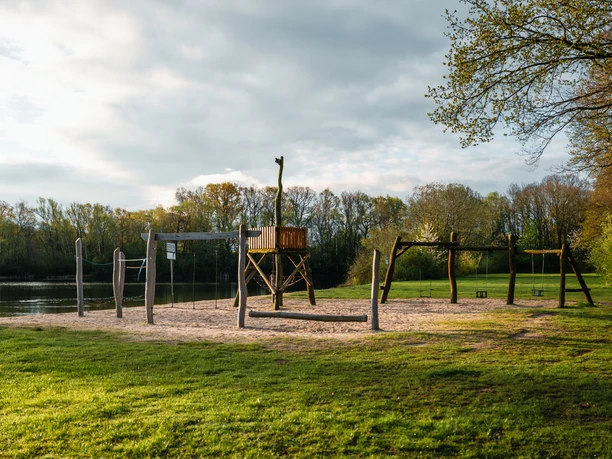 Badesee Mindenerwald Spielplatz am Badesee Mindenerwald mit Schaukeln und Rutsche, umgeben von grünen Wiesen und Bäumen.