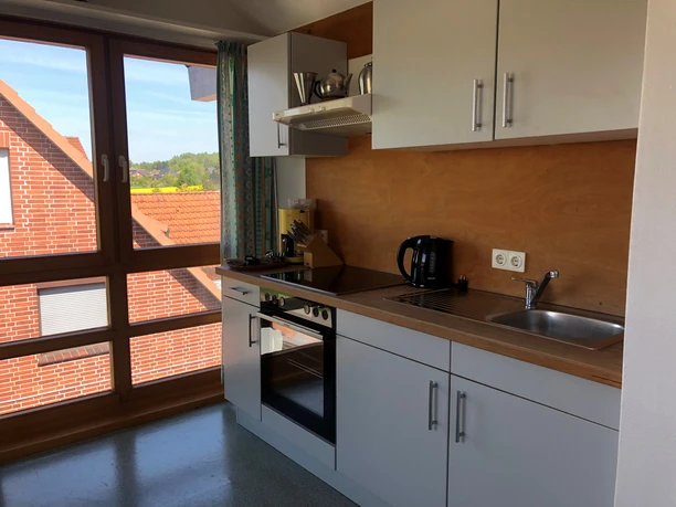 Compact kitchen with modern appliances, wooden elements and large window with a view of red tiled roofs.