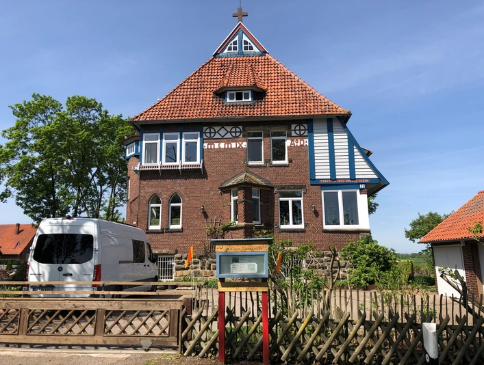 Pilgerherberge Altes Pfarrhaus Historisches rotes Backsteingebäude mit markantem Kreuzgiebeldach und weißen Fensterläden.Historic red brick building with striking cross-gabled roof and white shutters.Historisk rød murstensbygning med markant tværgående sadeltag og hvide skodder.Historisch gebouw van rode baksteen met opvallend zadeldak en witte luiken.