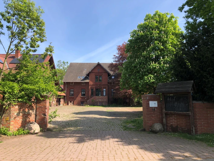 Hof Holthöfer Backsteinbau im ländlichen Stil mit gepflastertem Hof, umgeben von grünen Bäumen und gestrichenen Toren.
