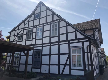 Gästezimmer Anna und Heini Fachwerkhaus mit weißen Wänden und dunklen Holzbalken, viele Fenster, ruhige Wohnlage, sonniger Tag.