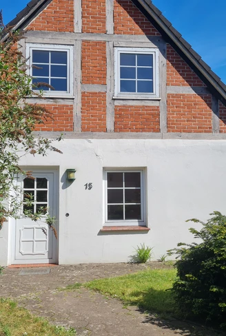 Fachwerkhaus mit roter Ziegelfassade, weißem Anstrich und einladendem Eingangsbereich im Grünen.Half-timbered house with red brick façade, white paint and inviting entrance area surrounded by greenery.Bindingsværkshus med rød murstensfacade, hvid maling og indbydende indgangsparti omgivet af grønt.Vakwerkhuis met rode bakstenen gevel, witte verf en uitnodigende entree omringd door groen.