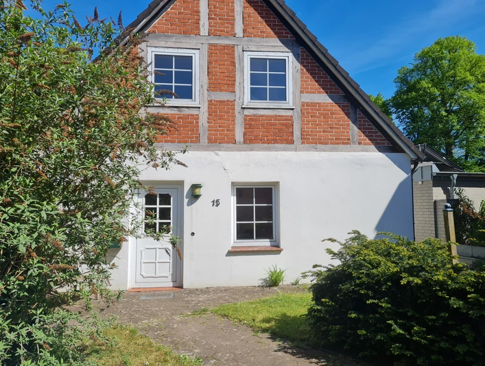 Fachwerkhaus mit roter Ziegelfassade, weißem Anstrich und einladendem Eingangsbereich im Grünen.