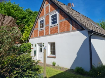 Ferienhaus Nienburg Fachwerkhaus mit roter Backsteinfassade und weißen Putzwänden, umgeben von gepflegtem Garten.
