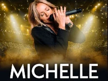 Michelle singt während ihrer Abschiedstournee auf einer Bühne im Schein goldener Lichter.