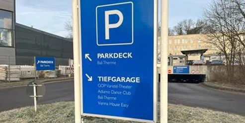 Parkhaus Morsbachallee.jpg Wegweiser zum Parkdeck und zur Tiefgarage, mit Hinweisen zu nahegelegenen Einrichtungen im Hintergrund.