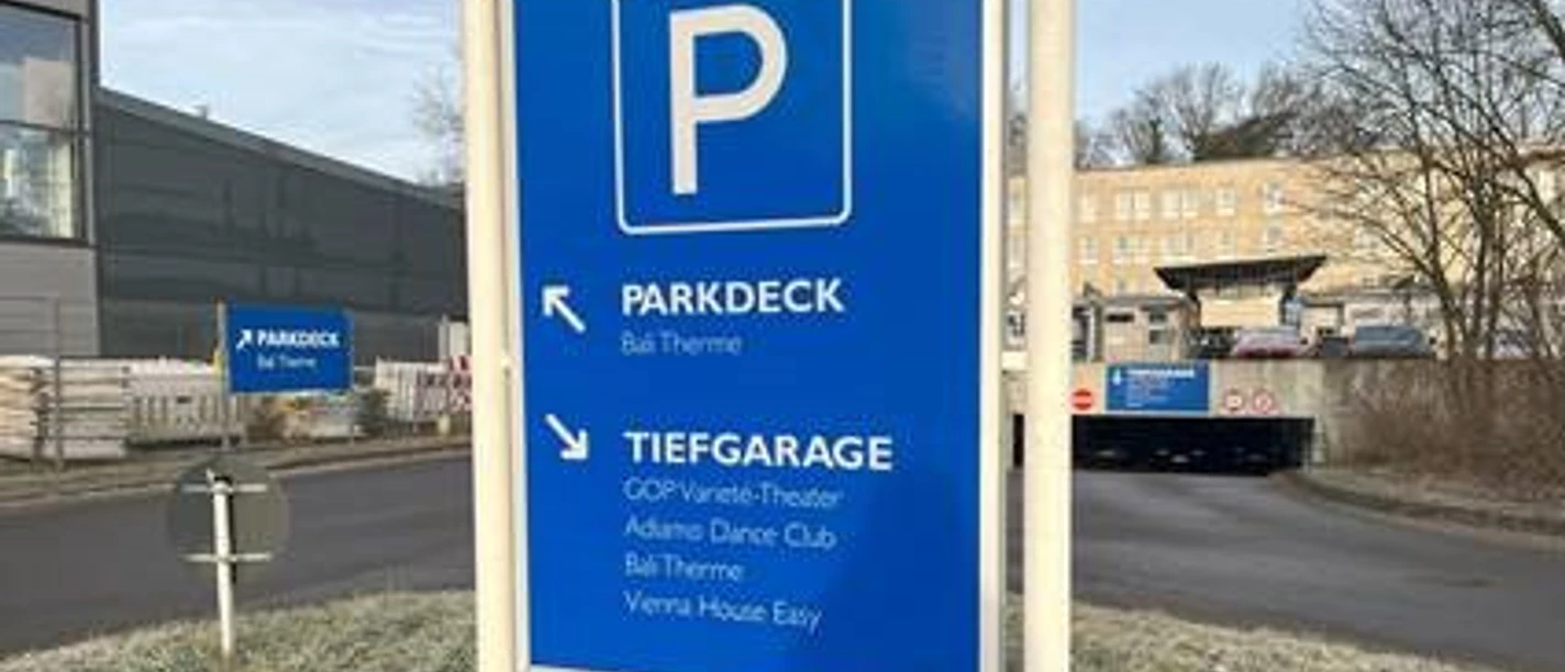 Parkhaus Morsbachallee.jpg Wegweiser zum Parkdeck und zur Tiefgarage, mit Hinweisen zu nahegelegenen Einrichtungen im Hintergrund.