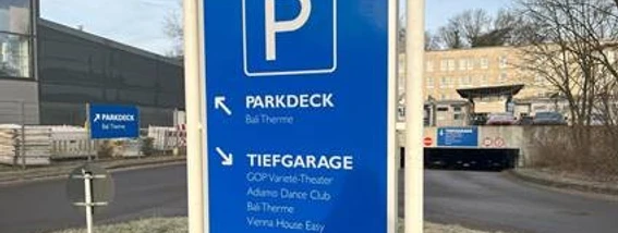 Parkhaus Morsbachallee.jpg Wegweiser zum Parkdeck und zur Tiefgarage, mit Hinweisen zu nahegelegenen Einrichtungen im Hintergrund.