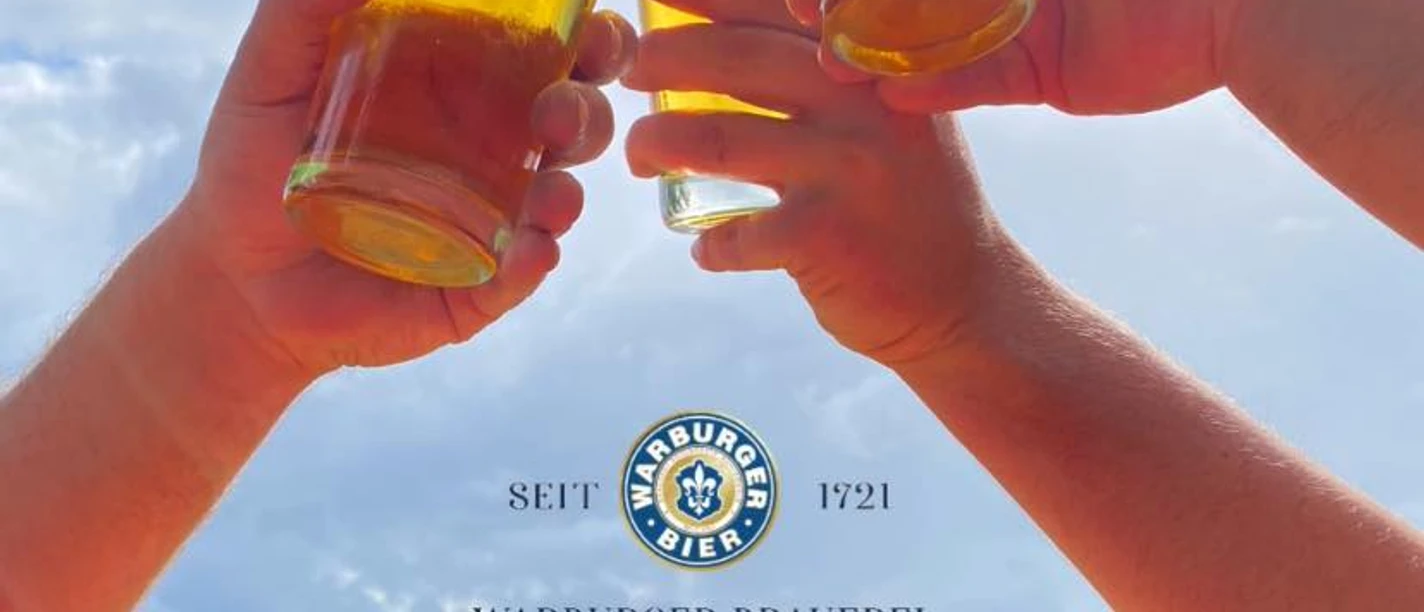 280688983_541883030869259_7393633277648066258_n.jpg Drei Hände stoßen mit halbvollen Biergläsern im Freien an; im Hintergrund sieht man den Himmel.