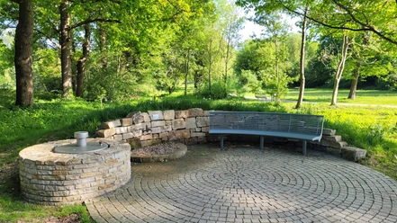 Kurpark Levern Runder Platz im Kurpark Levern mit Sitzbank und Brunneneinfassung, umgeben von grünen Bäumen.