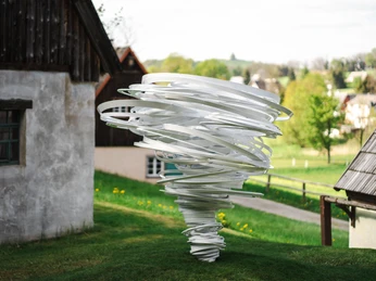 PurplePath_ TwisterAgain_Skulptur vor Wiese_quer_FotoErnestoUhlmann.jpg Eine weiße Skulptur in Spiralform steht auf einer Wiese, umgeben von Gebäuden und Bäumen.A white spiral-shaped sculpture stands on a meadow, surrounded by buildings and trees.Na louce obklopené budovami a stromy stojí bílá spirálovitá socha.Biała rzeźba w kształcie spirali stoi na łące, otoczona budynkami i drzewami.Een wit spiraalvormig beeld staat op een weiland, omringd door gebouwen en bomen.Una scultura bianca a forma di spirale si trova su un prato, circondata da edifici e alberi.