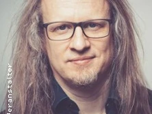 Porträt eines Mannes mit langen Haaren und Brille, lächelnd in die Kamera blickend. Moody Lighting.