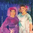 Zwei Drag Queens in farbenfrohen Kostümen und Perücken posieren vor einem glitzernden Hintergrund.