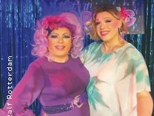 Zwei Drag Queens in farbenfrohen Kostümen und Perücken posieren vor einem glitzernden Hintergrund.